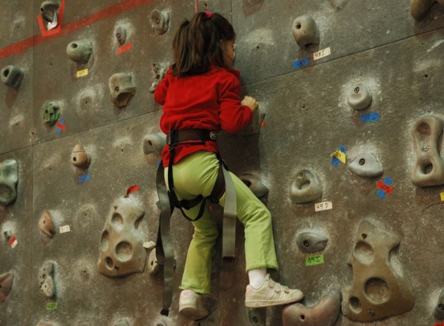 Bambina sulla parete da arrampicata con una felpa rossa 