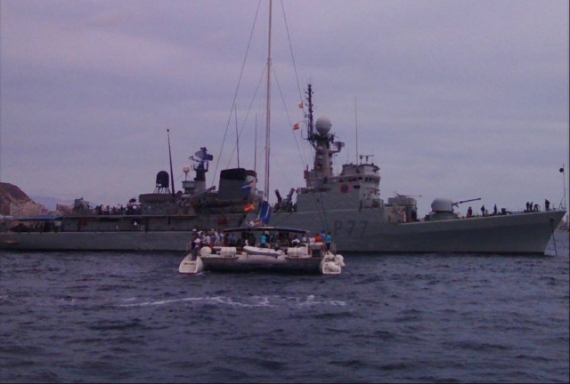 El catamarán fondeando la costa con un enorme carguero detrás