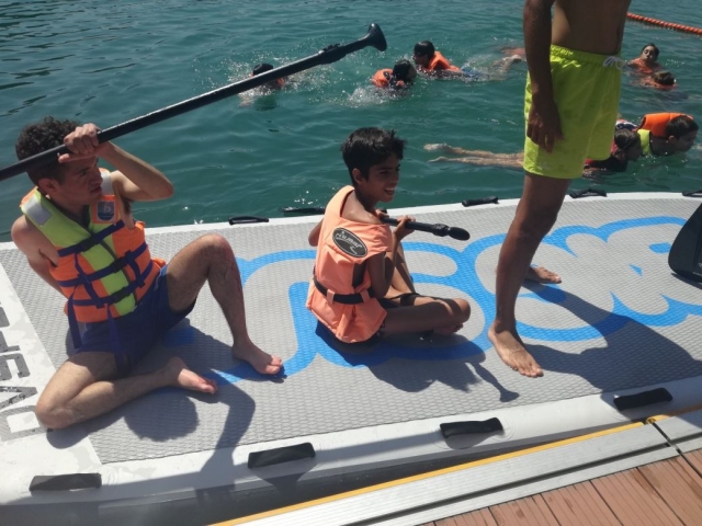  Due bambini seduti e un altro in piedi, riposato, sulla tavola da paddle surf surf 