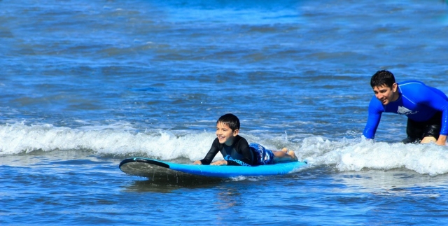 Niño aprendiendo a surfear junto al monitor