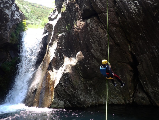  Un utente che scende in corda doppia lungo il fianco di una cascata 