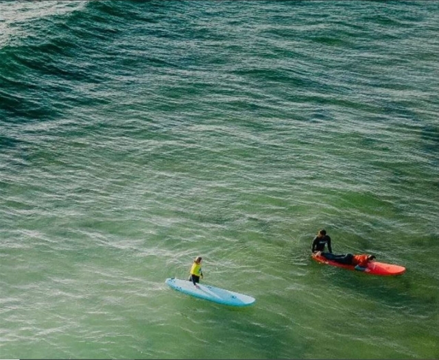  Due surfisti con tavole blu e rosse che entrano in acqua 
